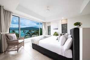 A modern hotel room with a large bed, a wicker chair, a view of the sea, and a balcony.