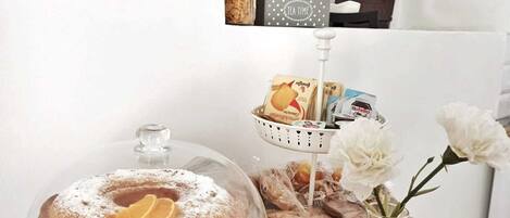 A dessert display with a covered cake, a basket of bread, and a vase with flowers on a wooden table.
