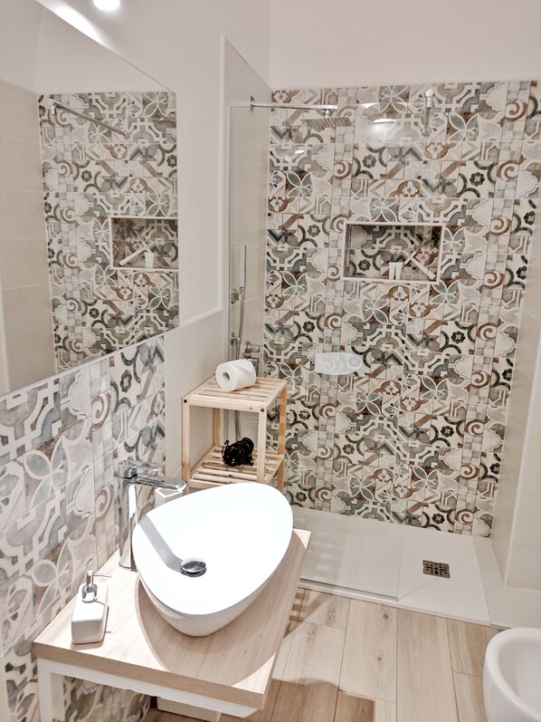 A modern bathroom with a large white sink, a shower area, and patterned tiles on the walls. - Loft in the historic center few steps from Ortigia (Siracusa)