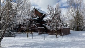 A snow-covered lodge with a wooden exterior, surrounded by snow-laden trees and a fenced yard. - 10 minutes to Slopes! Wild Turkey Lodge & Farm BnB, A 5-star traveler's dream! (Huntsville)