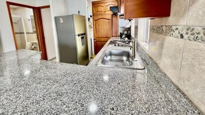 Une cuisine dotée de plans de travail en granit, d’un évier en acier inoxydable, de meubles en bois et d’un four encastré.