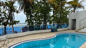 Une piscine dont le bord est revêtu de carrelage, entourée de palmiers et offrant une vue sur l’océan.