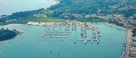 Vista aérea de uma marina com vários barcos atracados, rodeada por uma cidade costeira e vegetação.