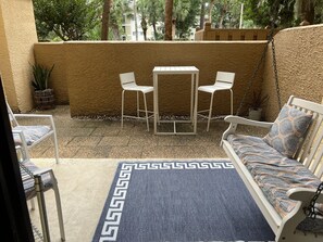A patio with a white table and chairs, a white sofa with patterned cushions, and a decorative rug.