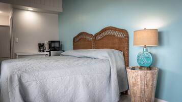 A neatly made bed with a patterned bedspread, a wicker headboard, a bedside lamp, and a coffee maker on a small table beside the bed.