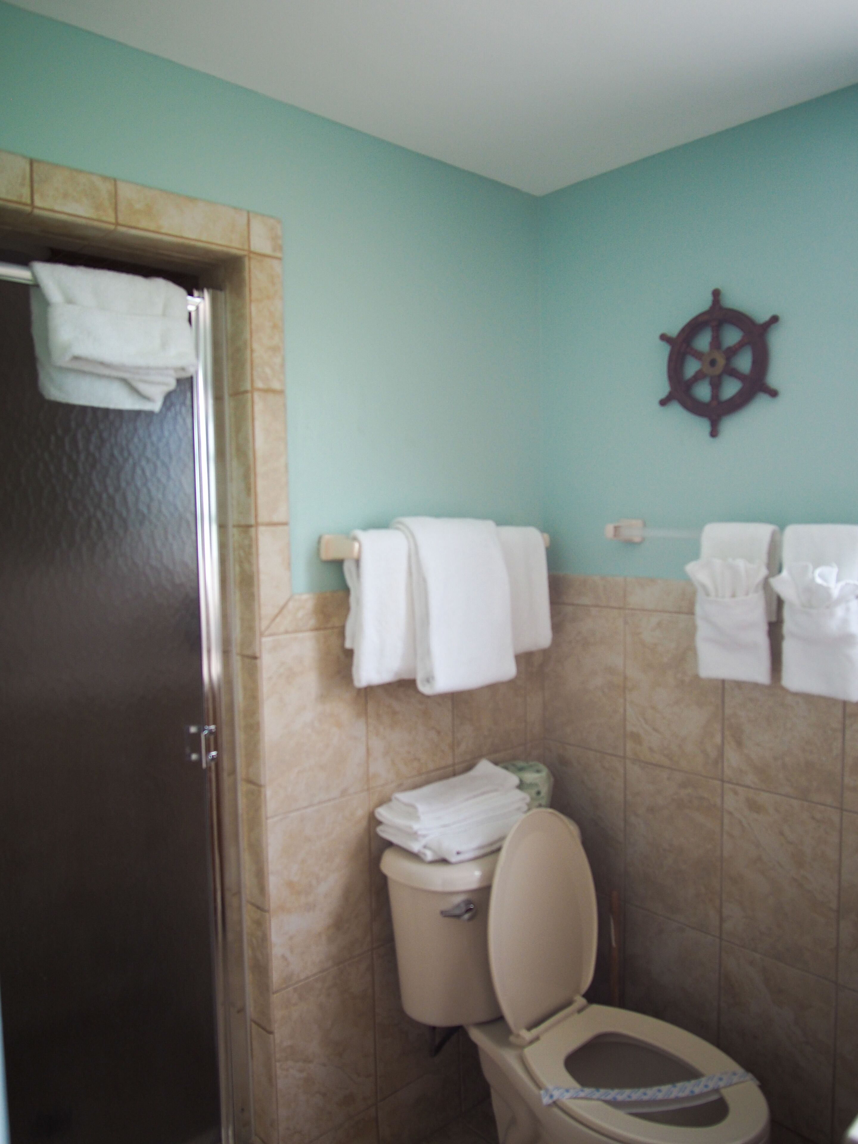 A bathroom with a toilet, a towel rack, and a ship's wheel decoration on the wall.