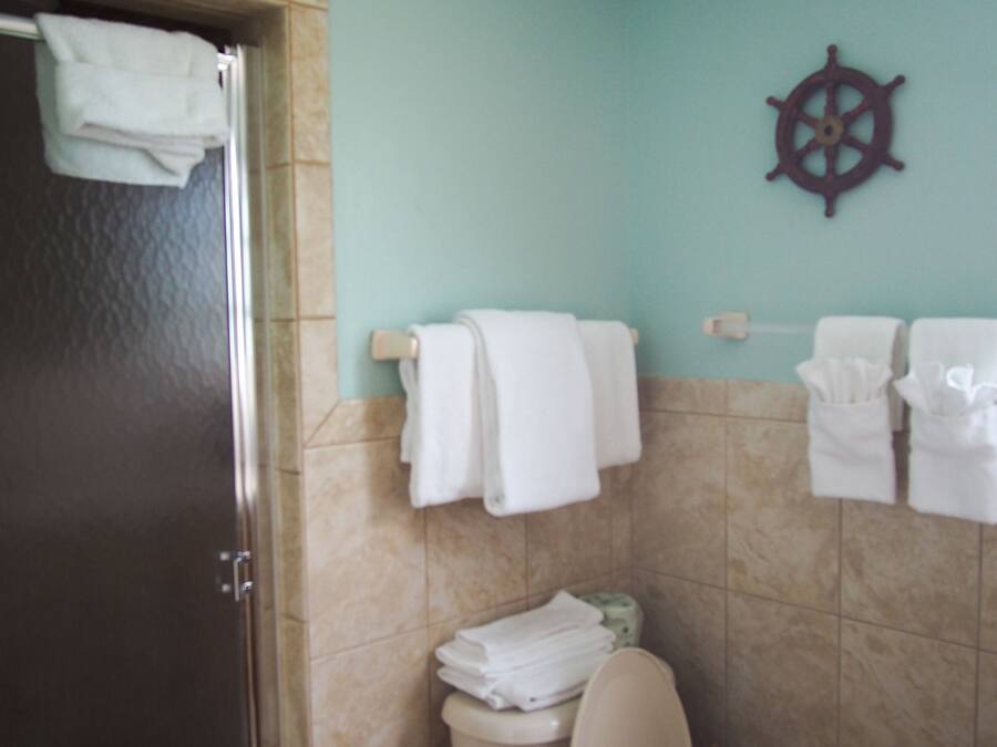 A bathroom with a toilet, a towel rack, and a ship's wheel decoration on the wall.