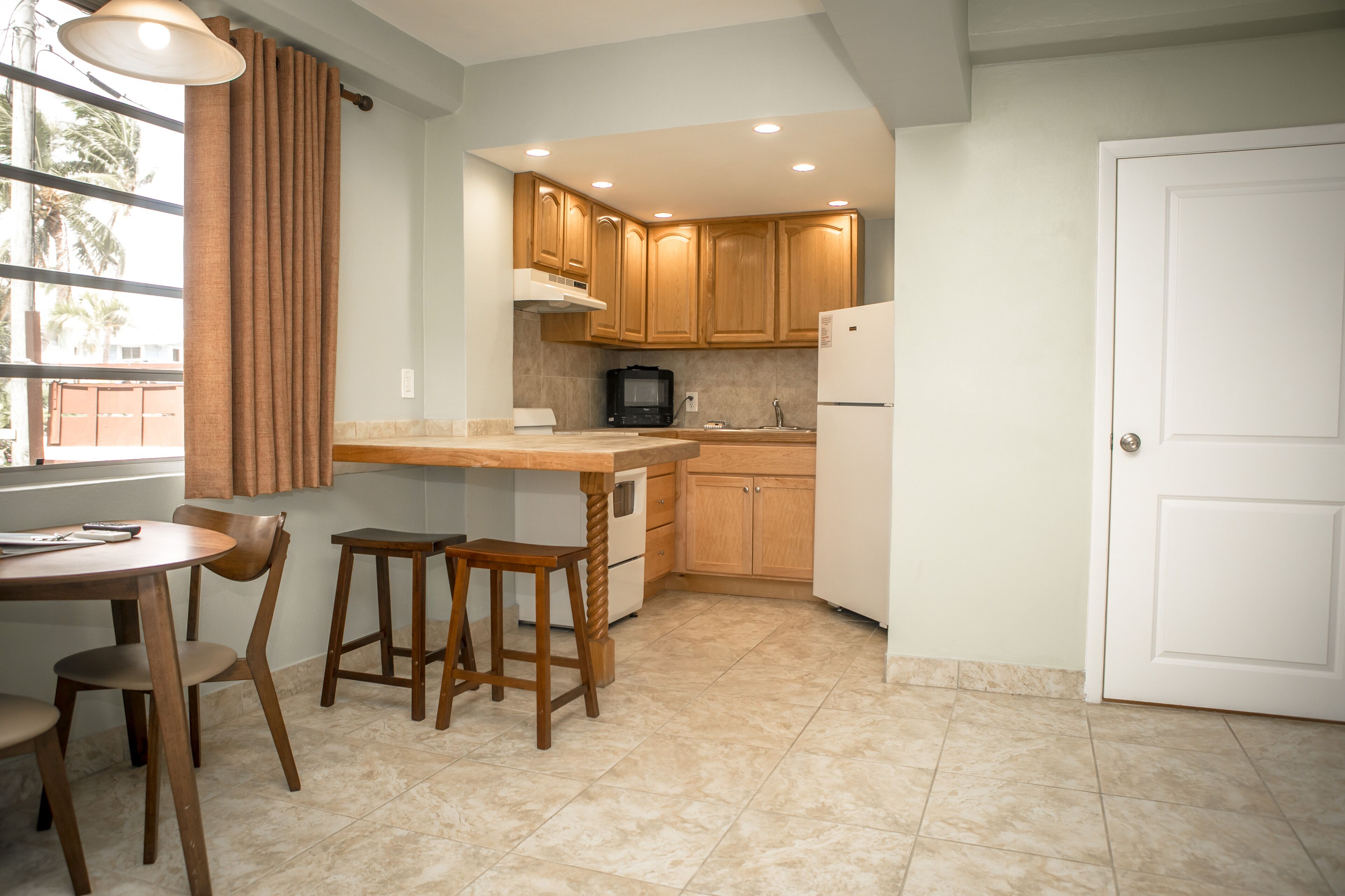 A kitchen with wooden cabinets, a white refrigerator, a microwave, and a dining area with a table and chairs.