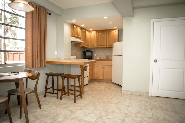 A kitchen with wooden cabinets, a white refrigerator, a microwave, and a dining area with a table and chairs. - Ragged Edge Resort & Marina (Islamorada)