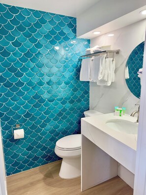 A bathroom with a white toilet, a sink with a mirror, and a wall with a blue scale pattern.