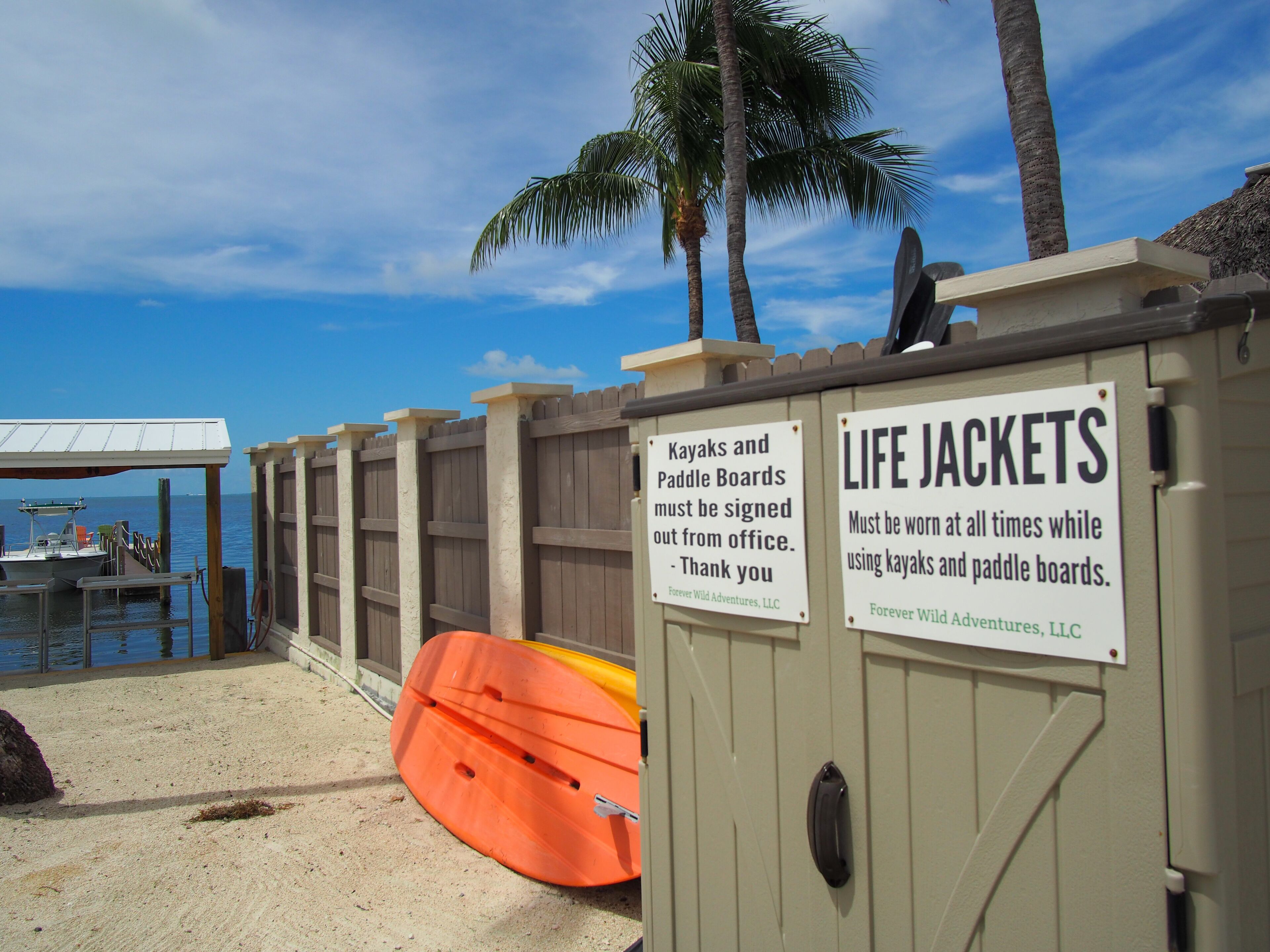 A wooden fence with signs indicating that kayaks and paddle boards must be signed out from the office and life jackets must be worn at all times while using them.