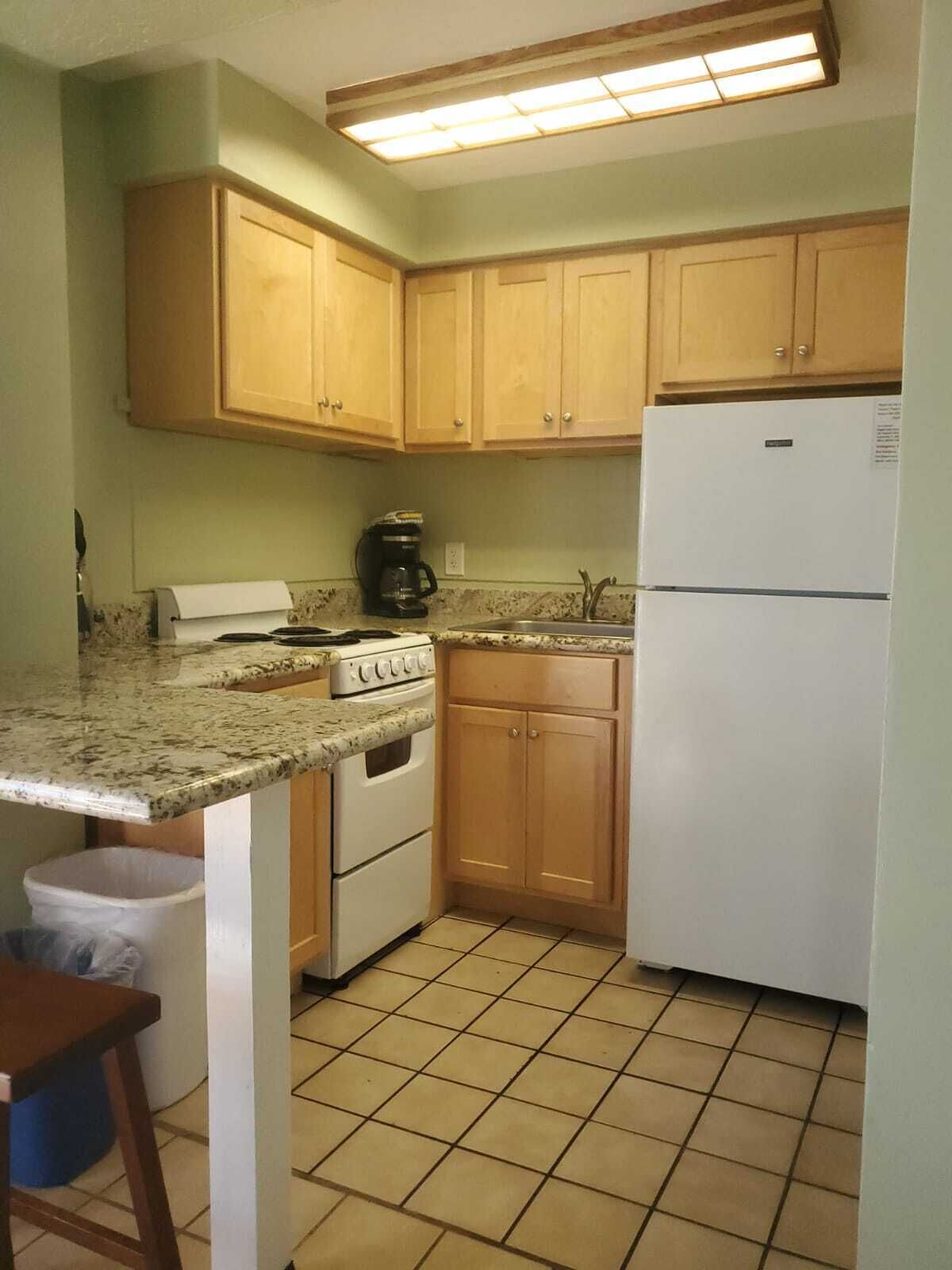 A kitchen with wooden cabinets, a white refrigerator, a coffee maker, and a stove.