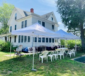 A large white house with a covered patio area featuring white plastic chairs and tables. - Winnisquam Lake House (Tilton)