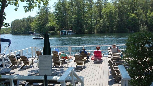 Une terrasse en bois, agrémentée de chaises et de tables, donnant sur un lac, avec un panneau indiquant les règles et les consignes à respecter.