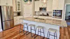 A modern kitchen with white cabinetry, stainless steel appliances, granite countertops, and bar stools. - Coastal Club * 6BR Lewes Beach House (Lewes)