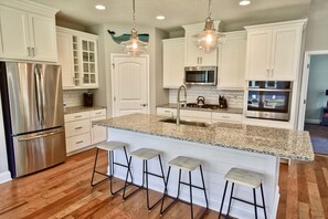 Una cocina moderna con armarios blancos, electrodomésticos de acero inoxidable, encimeras de granito y taburetes de bar.