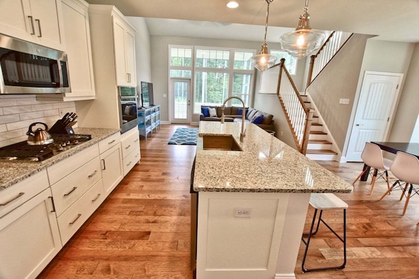 A kitchen with granite countertops, white cabinetry, a built-in oven, and a large island with a sink.