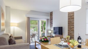 A modern hotel room with a sofa, dining table, and a TV. - Superior 1-Bed Villa | Quinta do Lago | Sleeps 4 (Almancil)