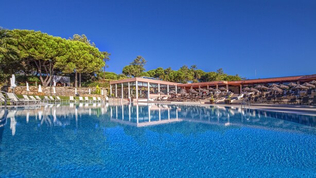 A clear blue pool with lounge chairs and umbrellas, surrounded by trees and a covered area. - Premium 2-Bed Villa | Quinta do Lago | Sleeps 6 (Almancil)
