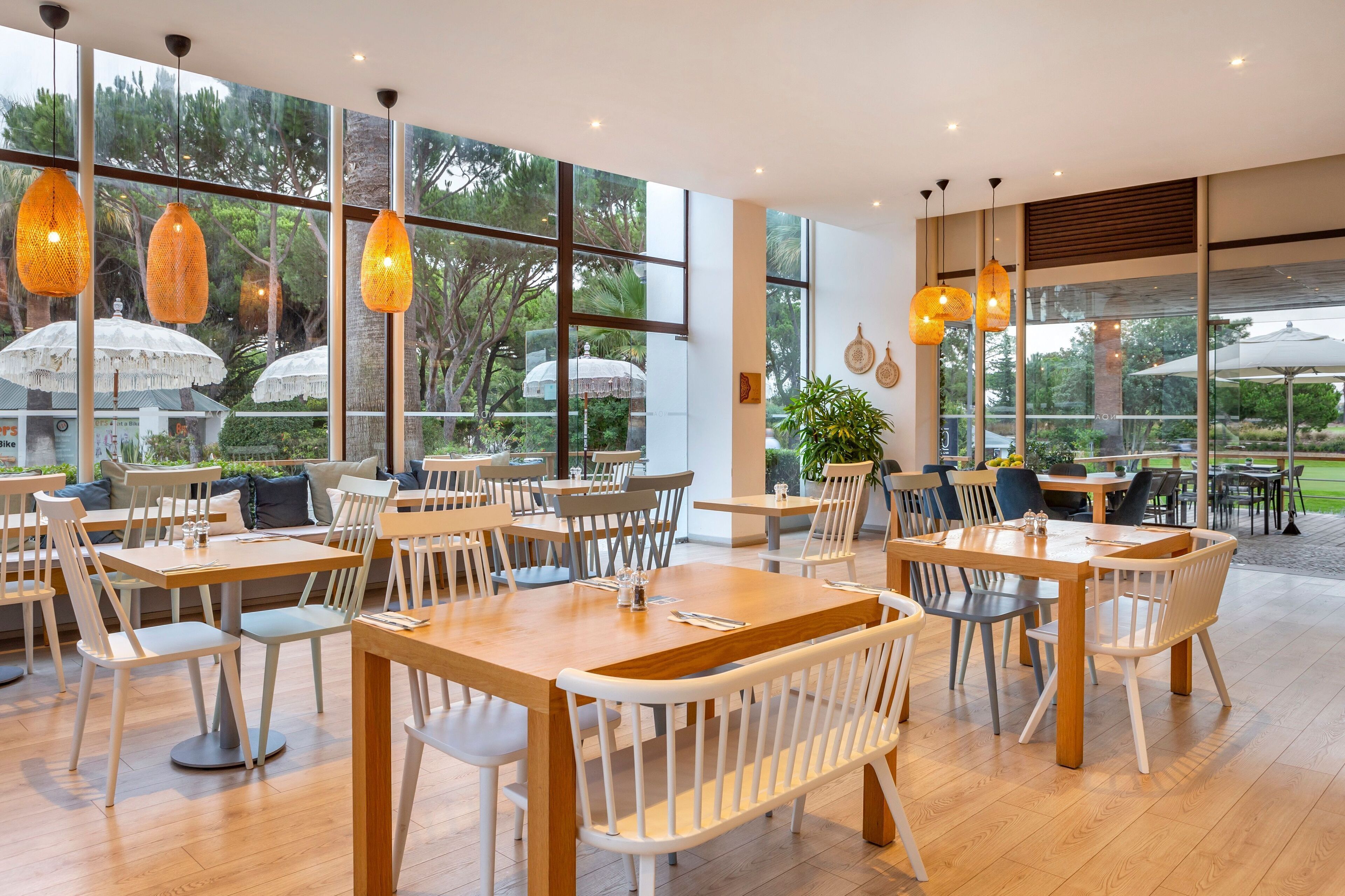 Un vaste espace de restauration intérieur, doté de grandes fenêtres, de tables en bois et de chaises blanches.