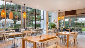 A spacious indoor dining area with large windows, wooden tables, and white chairs. - Premium 2-Bed Villa | Quinta do Lago | Sleeps 6 (Almancil)