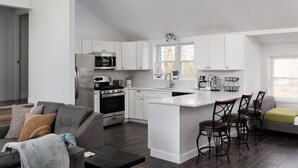 Una cocina moderna con armarios blancos, una isla central, taburetes de bar y un comedor.