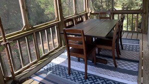A covered patio with a wooden table and chairs, large windows, and patterned floor mats. - JD36: Flyway | Multiple Decks with Amazing Marsh Views (Ocracoke)