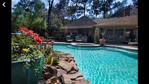A swimming pool with a stone border, surrounded by potted plants and a building with a sloped roof. - Houston Hidden Oasis (Spring)