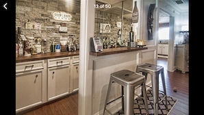 A kitchen with a stone backsplash, bar stools, and a variety of kitchen appliances. - Houston Hidden Oasis (Spring)