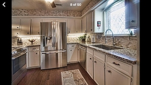 A modern kitchen with stainless steel appliances, a granite countertop, and a window with blinds. - Houston Hidden Oasis (Spring)