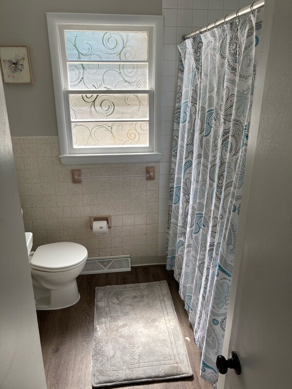Un bagno con il water, una finestra con vetro decorativo, una tenda da doccia con motivo paisley e un pavimento in legno.
