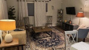 Una sala de estar con un sofá, dos sillones, una mesa de centro, un televisor, una lámpara y una alfombra estampada.