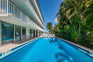 Une piscine à l’eau d’un bleu cristallin, entourée d’un bâtiment moderne doté de grandes fenêtres et d’un balcon.
