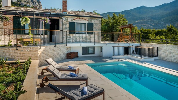 Une villa moderne dotée d’une piscine, de murs en pierre et d’un balcon offrant une vue sur un paysage montagneux.