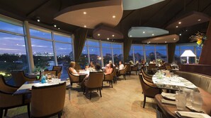 A restaurant with tables set for dining, large windows offering a view of the cityscape, and a modern interior design.