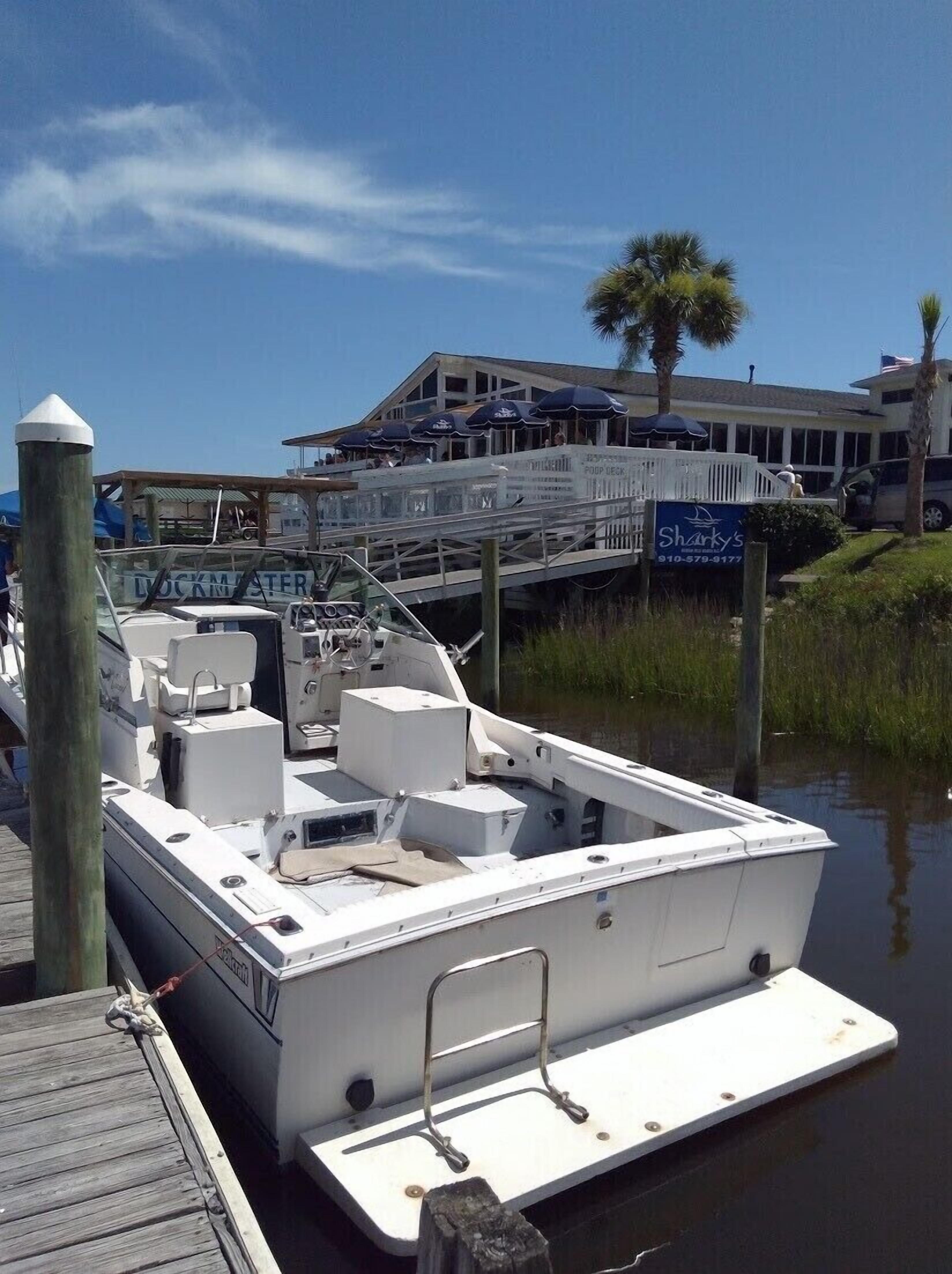 A docked boat with a cabin, a wooden pier, and a building with a sign for 'Sharky's' in the background.