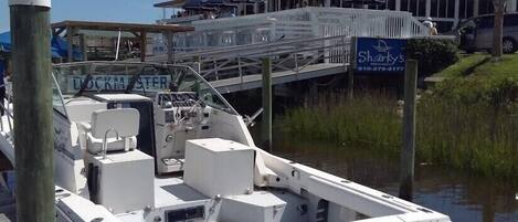 A docked boat with a cabin, a wooden pier, and a building with a sign for 'Sharky's' in the background.