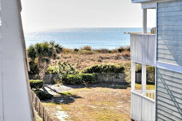 A view of a beachside property with a fenced yard and a wooden deck. - Condo with Ocean Views! Steps to the Sea! Sleeps 8. The complex is oceanfront! (Ocean Isle Beach)
