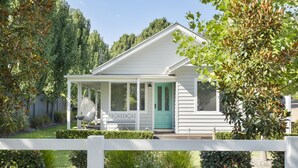 A white house with a green door, a porch, and a white fence in the foreground.