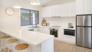 A modern kitchen with white cabinetry, a stainless steel refrigerator, a built-in oven, a microwave, and a large window providing natural light.