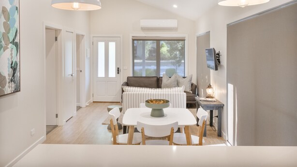 A modern living room with a sofa, dining table, and chairs. There is a window with a view of the outdoors.