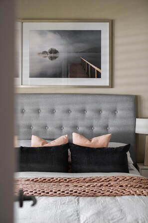 A bedroom with a tufted headboard, a framed picture above the bed, and a bedside lamp. - Three Sisters - Three Sisters has been designed and renovated with a strong appreciation of its surrounds and the importance of spending time with your nearest and dearest. (Bright)