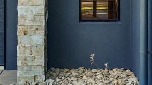 A modern building with a stone facade, a large window, and a small garden area with pebbles and plants.