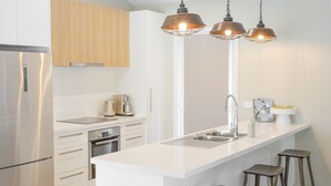 Una cocina moderna con armarios blancos, electrodomésticos de acero inoxidable, una isla central con taburetes e iluminación colgante.