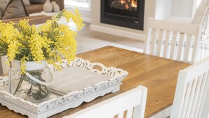 Una mesa de comedor con una bandeja blanca, un jarrón con flores amarillas y una chimenea al fondo.