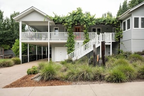 Une maison à deux étages dotée d’un porche couvert, d’un escalier et d’un jardin où poussent différentes espèces de plantes.