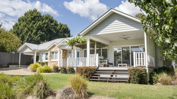 A two-story house with a covered porch, a stone foundation, and a well-maintained lawn.