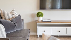 A living room with a grey sofa, white console table, and a flat-screen TV mounted on the wall.