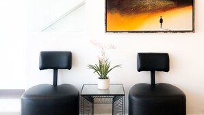 Una habitación moderna con dos otomanes negros, una mesita con una planta en maceta y un cuadro abstracto grande en la pared.