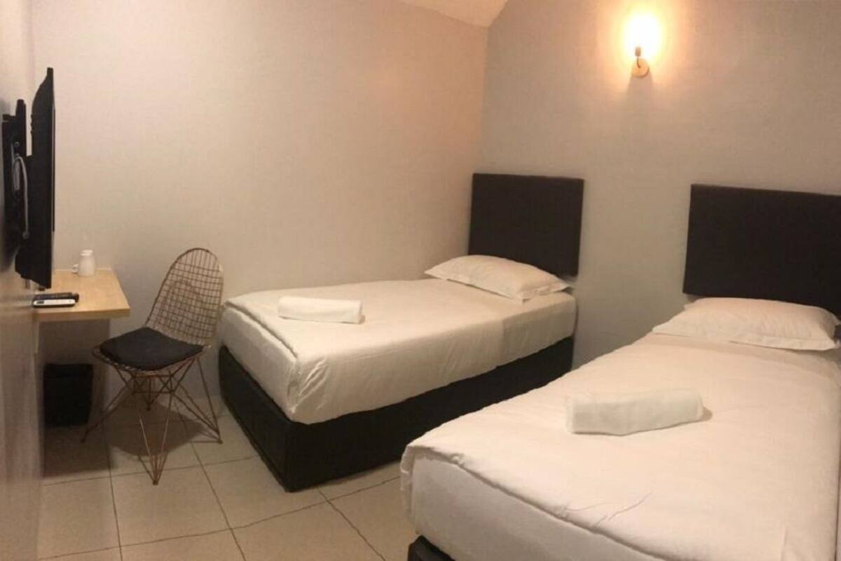 Ein Hotelzimmer mit zwei Einzelbetten, einem Schreibtisch mit Stuhl, einem Flachbildfernseher und einer Wandleuchte.